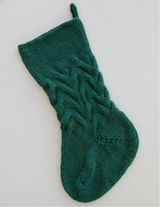 Green hand knitted cable christmas stocking on a light gray background
